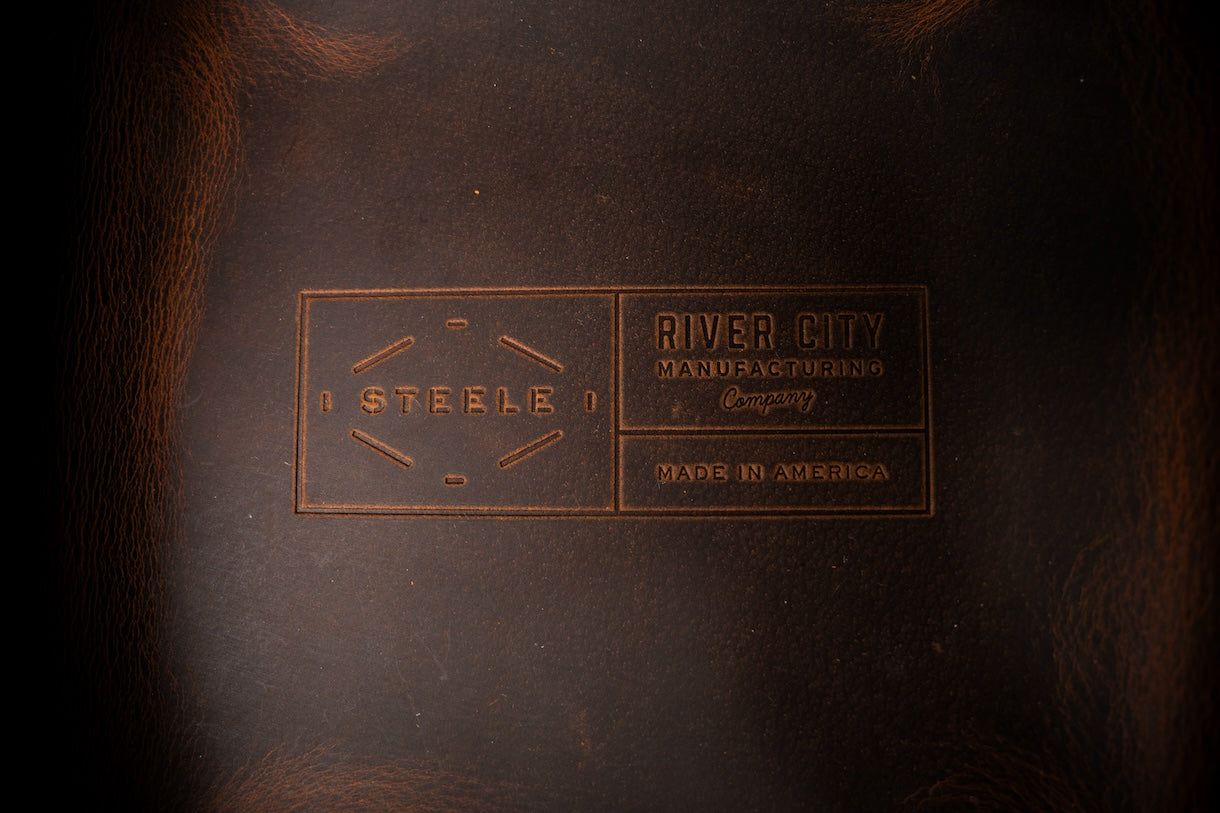 Close-up of a leather product with 'River City' branding on a dark background