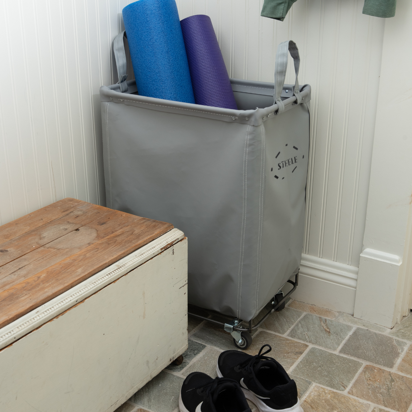 Gray laundry basket with rolled-up mats against a white wall.