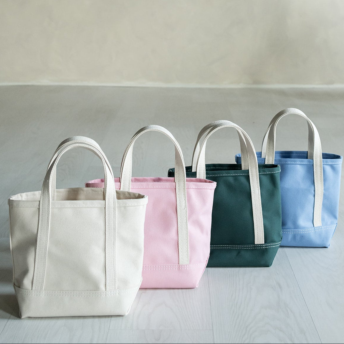 Four tote bags in different colors arranged on a light surface with a neutral background