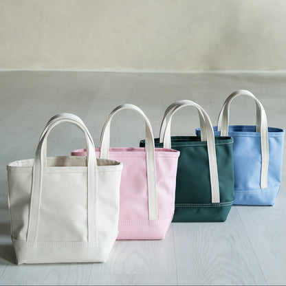 Four tote bags in different colors arranged on a light surface with a neutral background