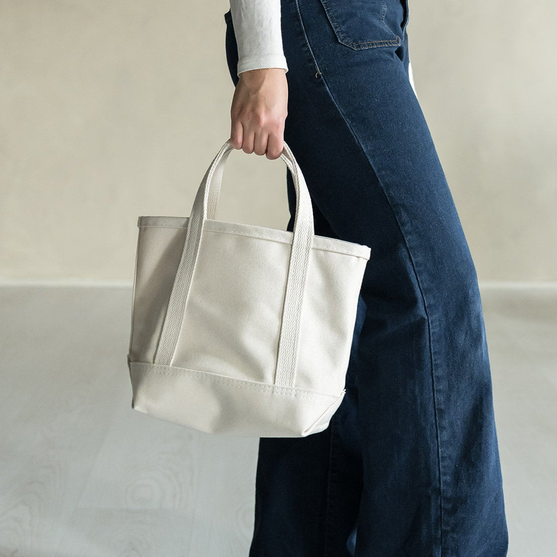 Person holding a natural canvas tote bag against a neutral background