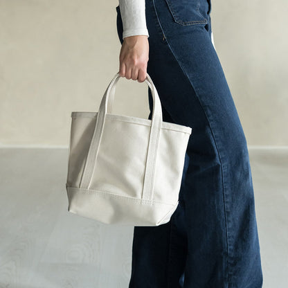 Person holding a natural canvas tote bag against a neutral background
