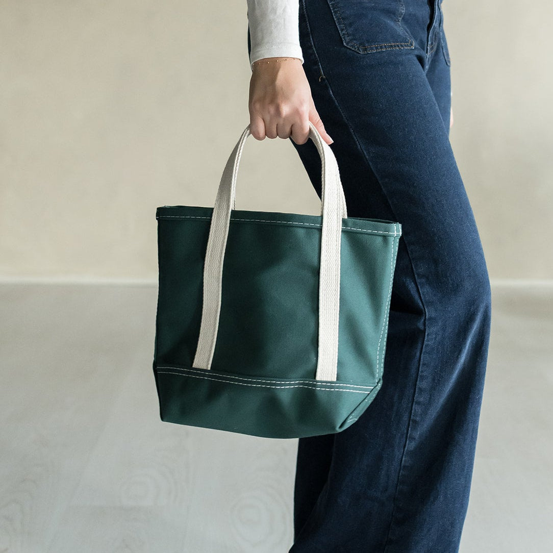 Person holding a green tote bag with white handles on a plain background