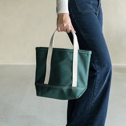 Person holding a green tote bag with white handles on a plain background
