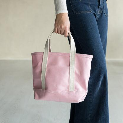 Person holding a pink tote bag with white handles on a plain background