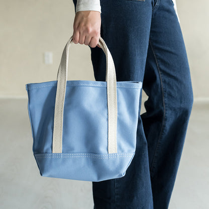 Person holding a blue tote bag with white handles against a neutral background