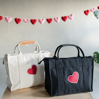 a black and natural canvas tote with heart patches standing next to eachother