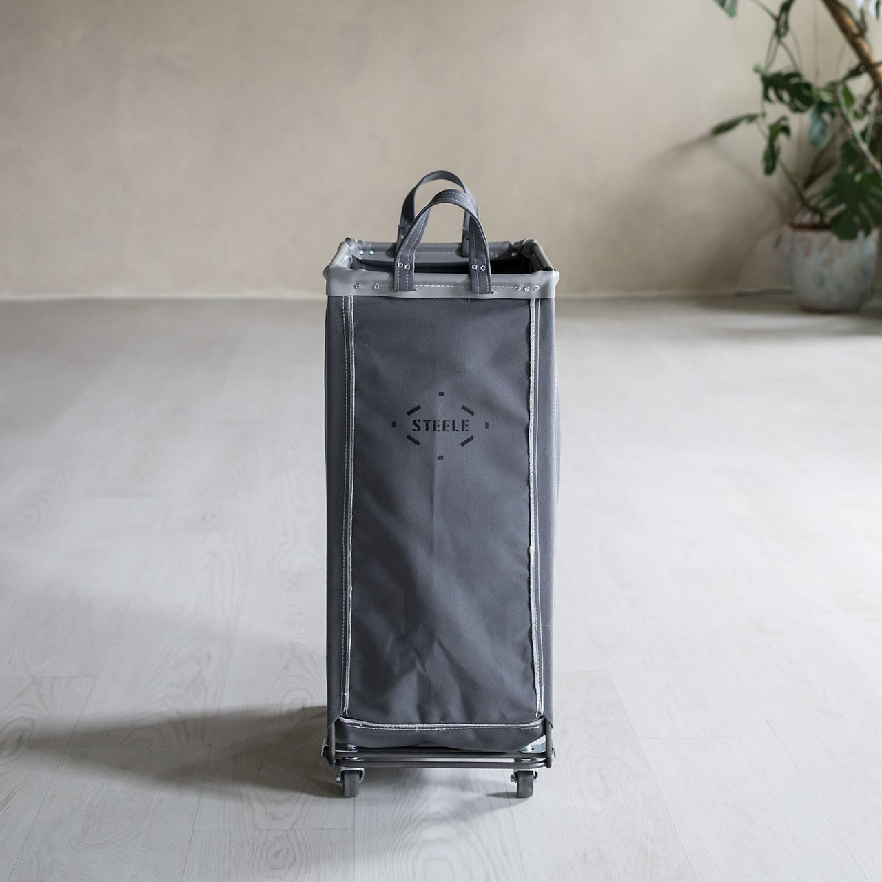 Gray rolling cart with 'STEELE' branding on a light surface with a plant in the background.