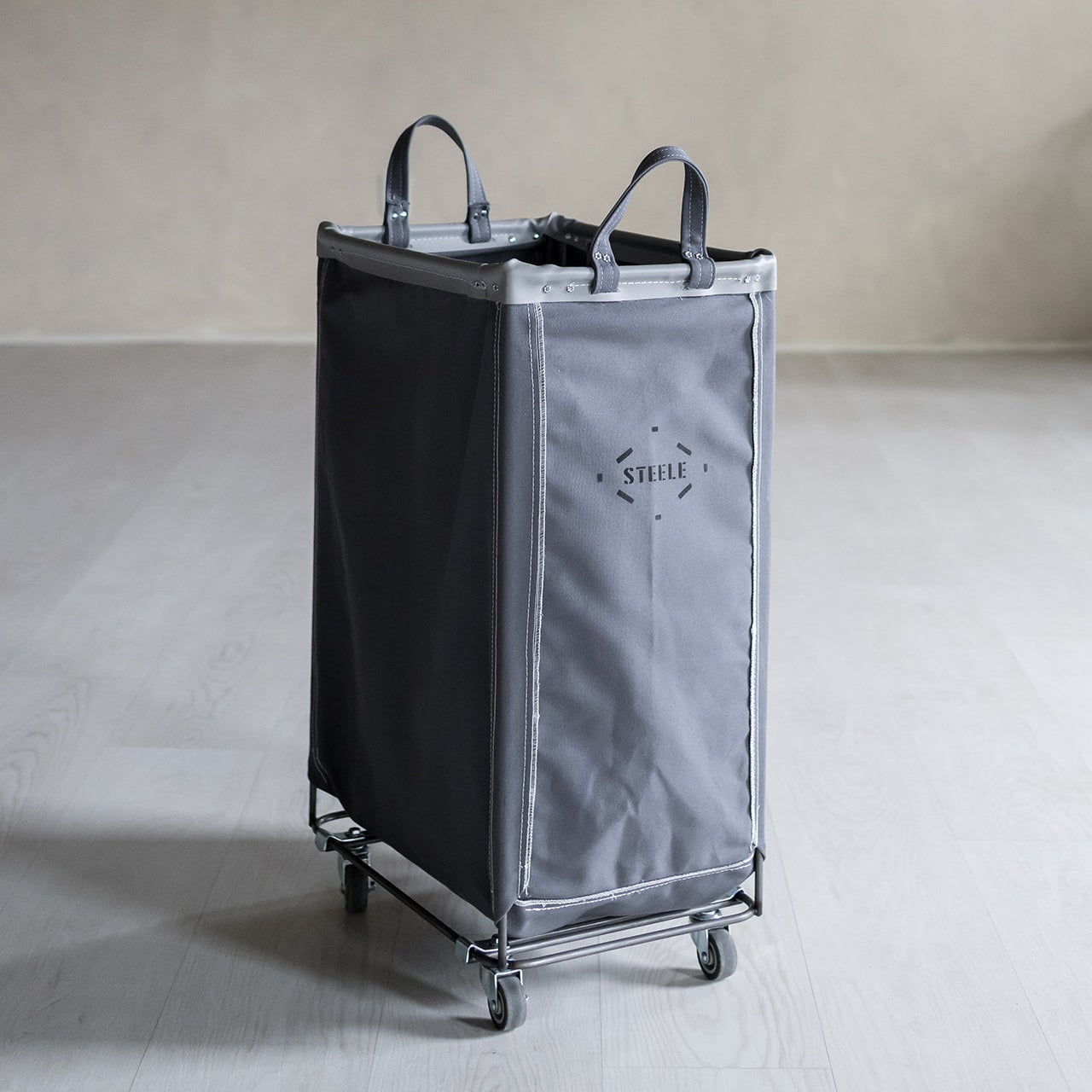 Gray laundry cart with wheels on a light gray floor against a beige wall