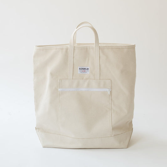 A light beige canvas tote bag with a front zippered pocket and a small white brand label, photographed against a plain off-white background.
