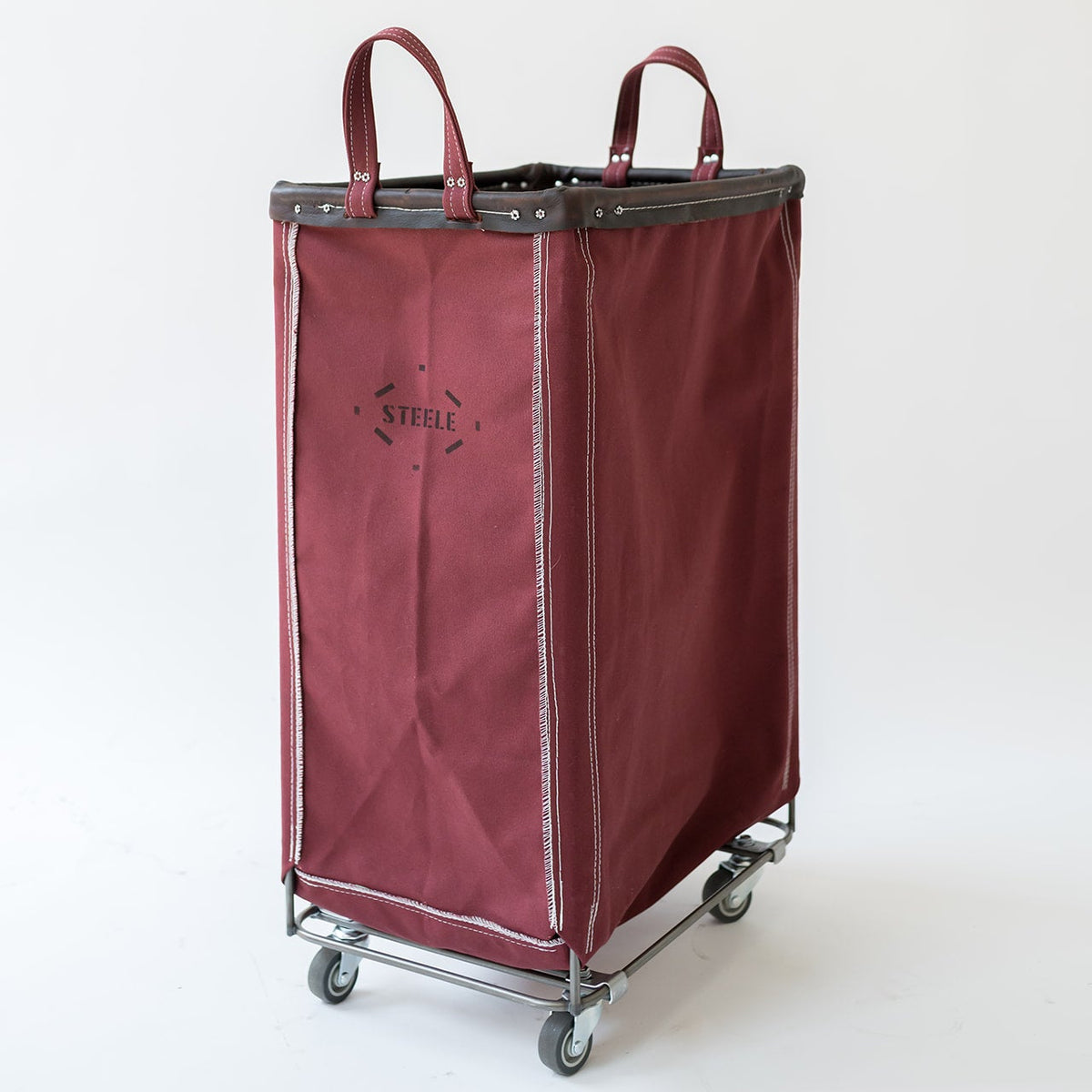 A burgundy fabric laundry hamper with dark gray trim and handles, mounted on a metal rolling cart with gray wheels. The brand name 'STELLE' is printed on the front.