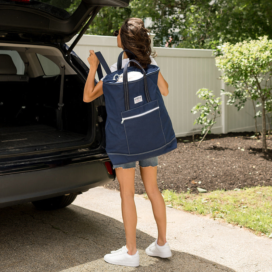 Person with a large blue backpack standing next to an open car trunk outdoors.