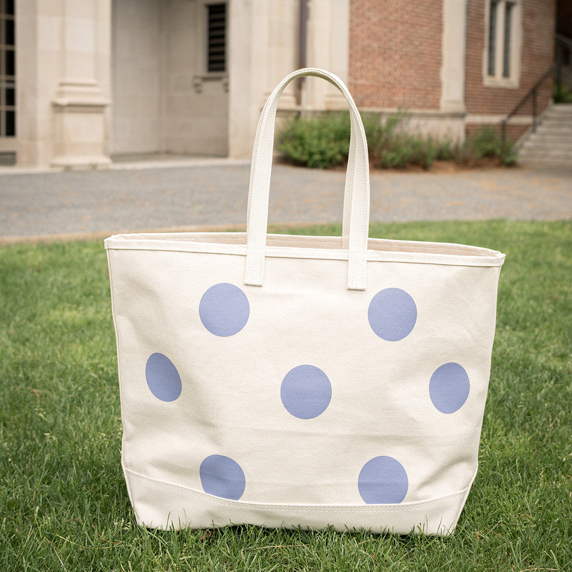 White tote bag with blue polka dots on grass in front of a building