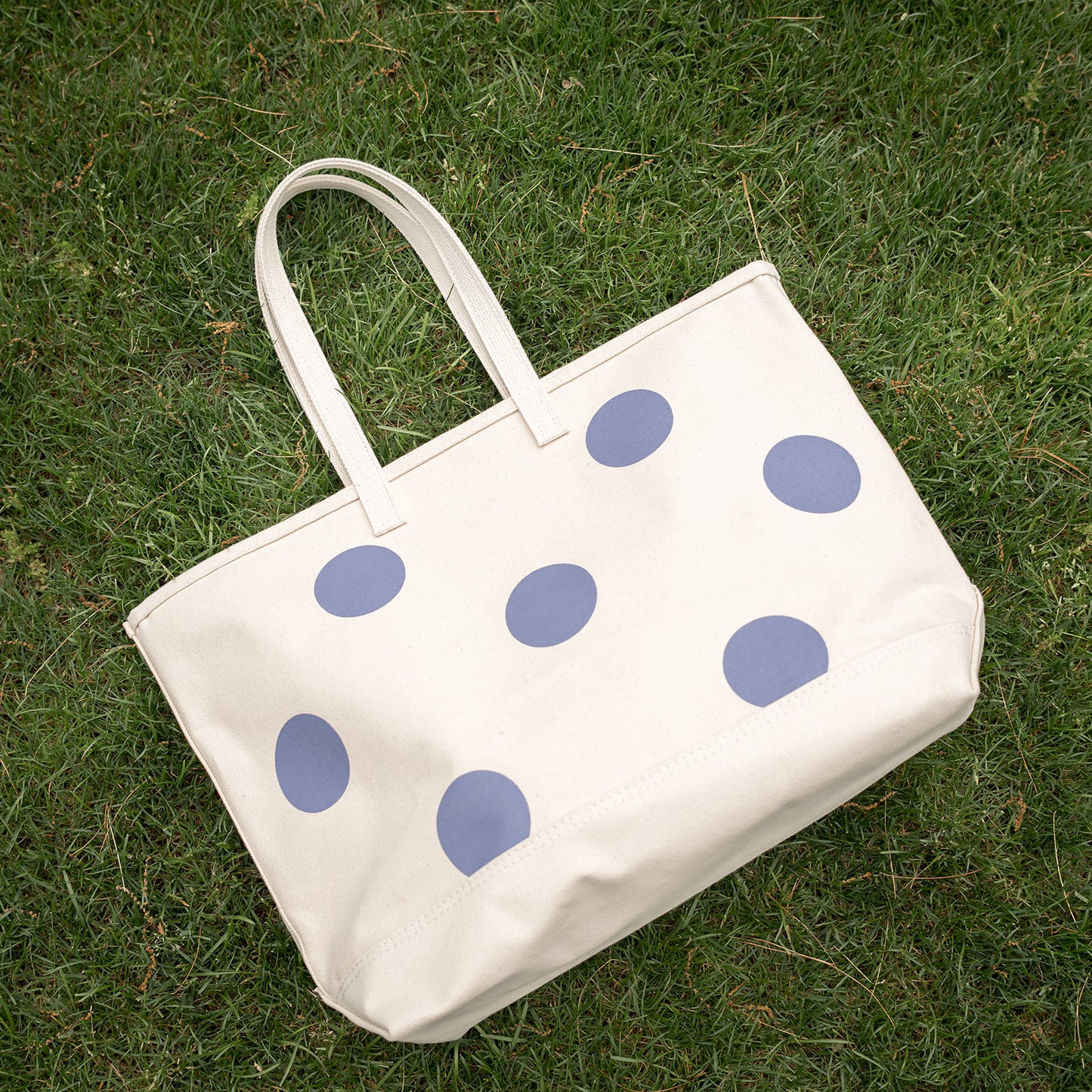 White tote bag with blue polka dots on grass