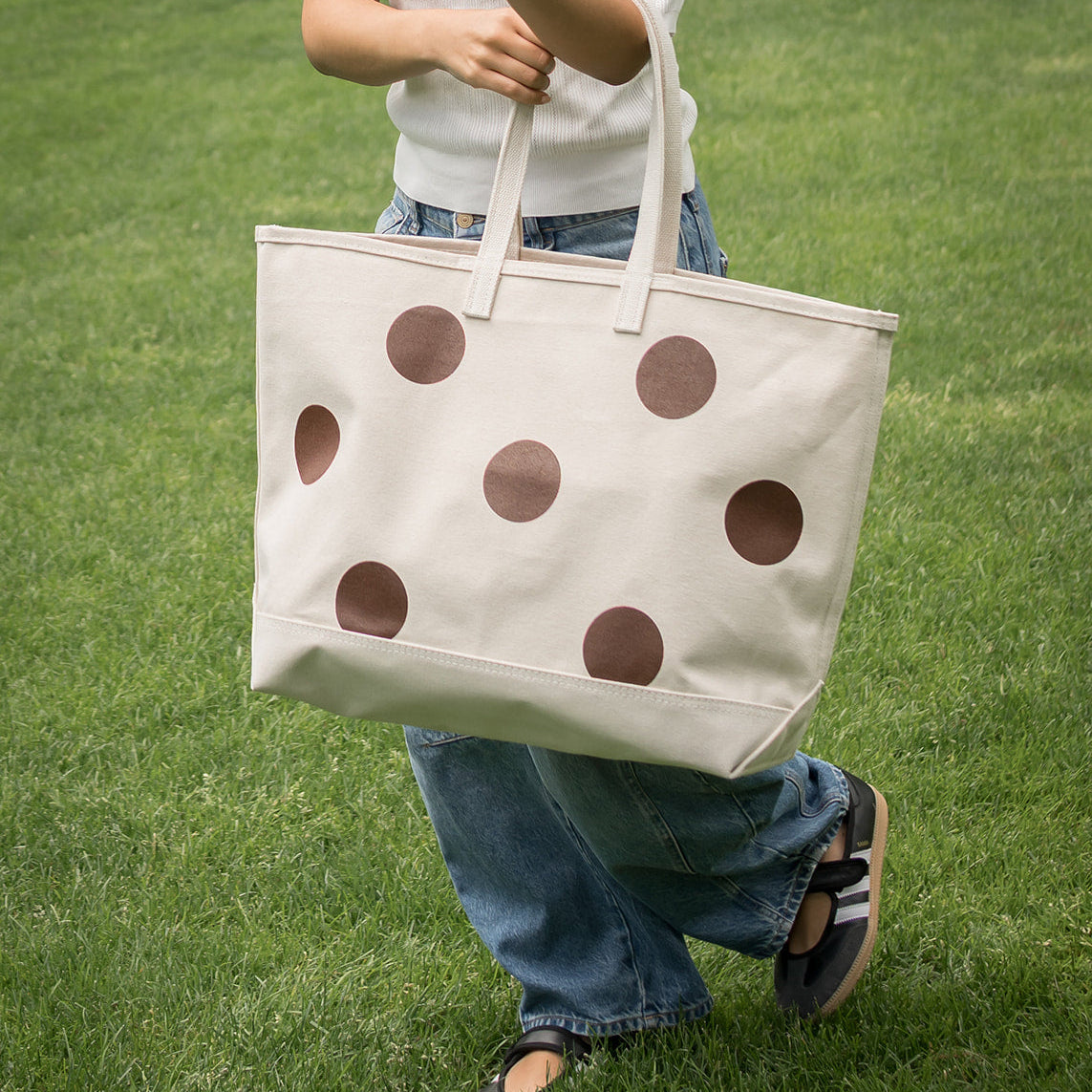 Person holding a beige tote bag with brown polka dots on grass