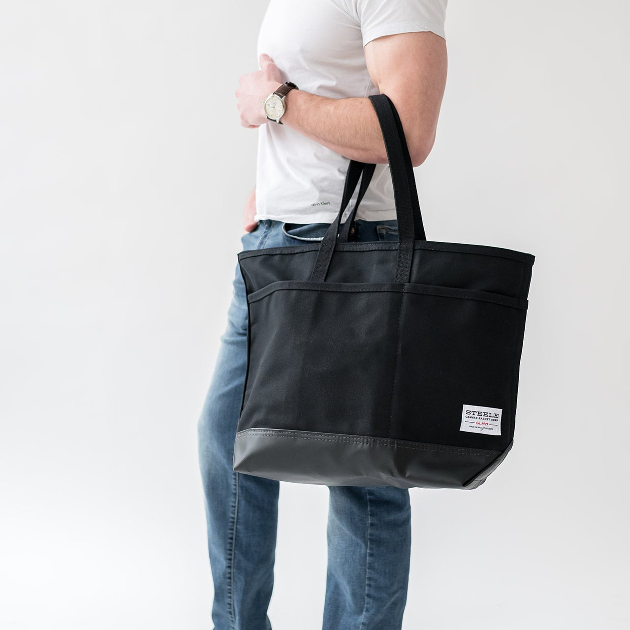 Person holding a black tote bag with a visible brand label on a white background