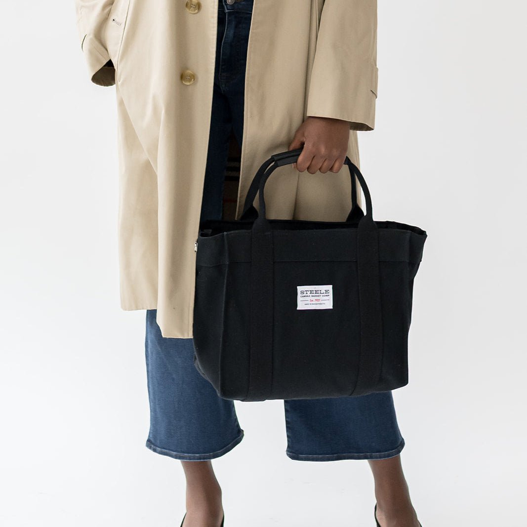 Person holding a black tote bag with a visible brand label on a white background