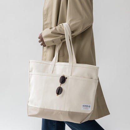 Person holding a beige tote bag with sunglasses on a plain background
