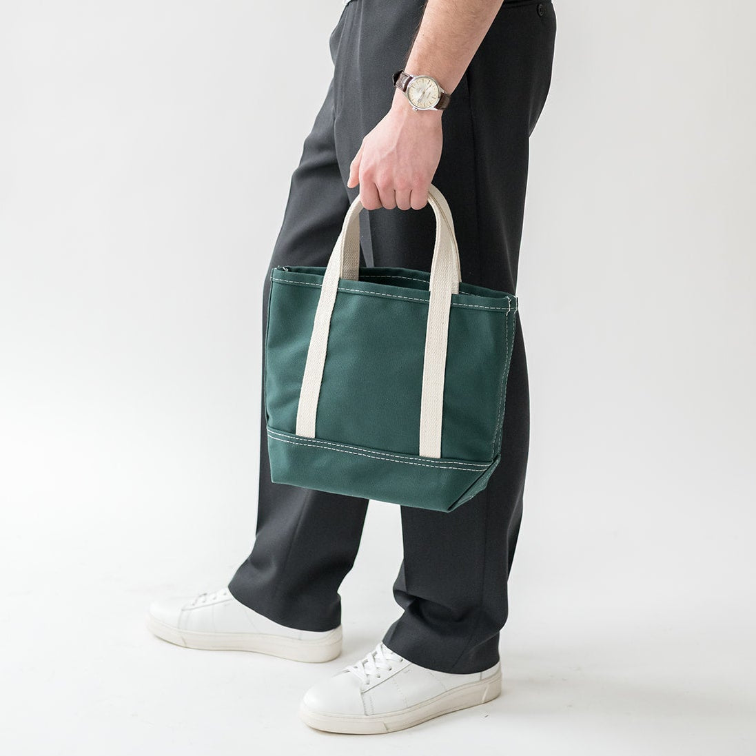 Person holding a green tote bag with white handles against a plain background