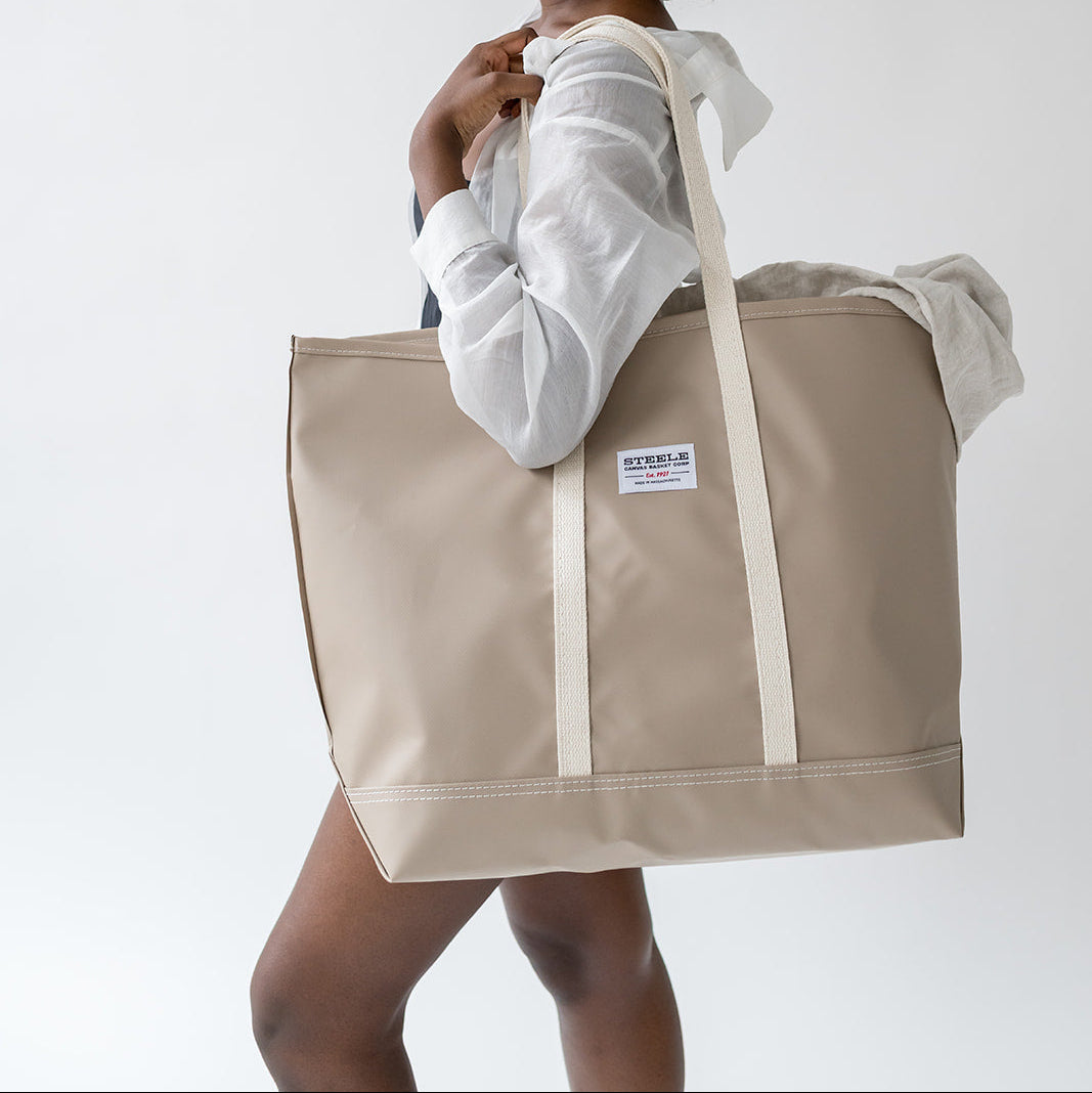 Woman holding a beige tote bag with a visible brand logo on a white background
