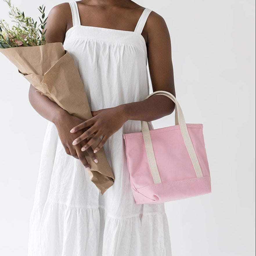 Woman in a white dress holding flowers and a pink bag on a white background