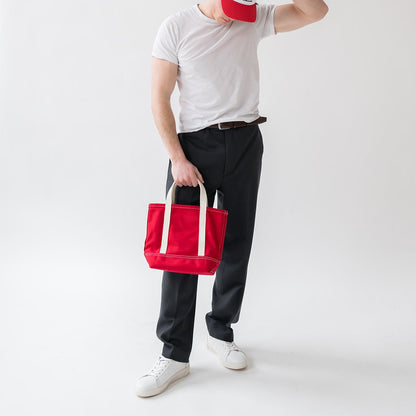 Person holding a red tote bag against a white background