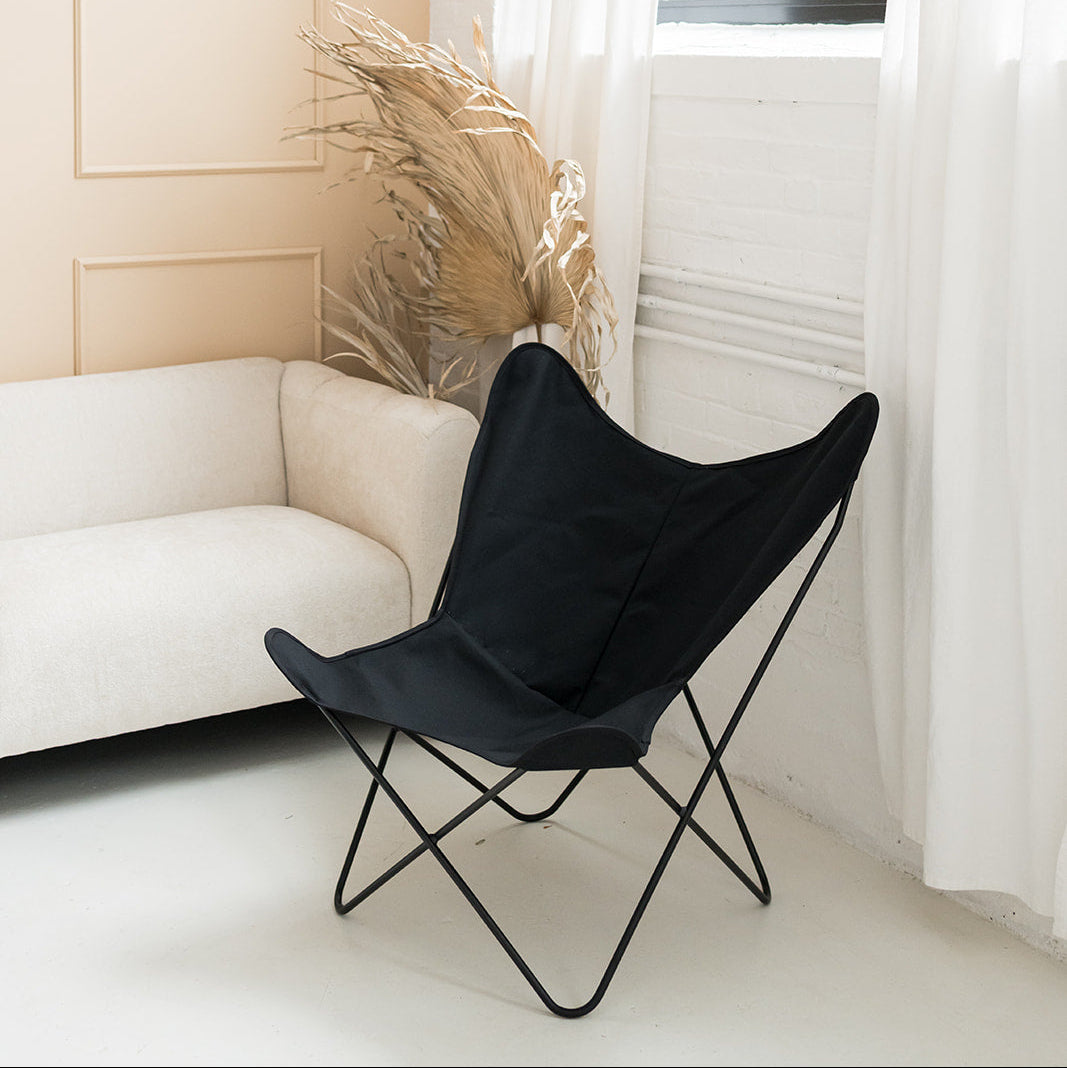 Black butterfly chair in a bright room with white curtains and a white sofa.
