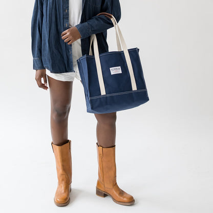 Person holding a navy tote bag with a white label on a white background