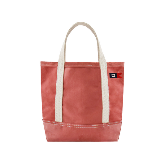 A nantucket red canvas tote bag with cream-colored woven handles and a small black and red square logo patch on the upper right side, shown against a plain white background.