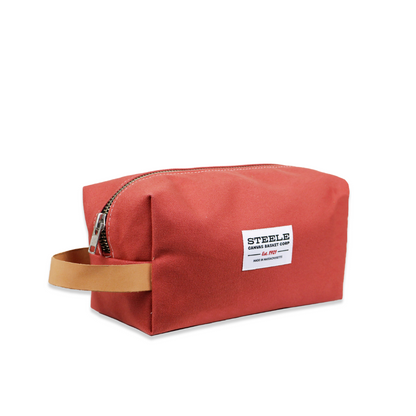 Red toiletry bag with a brown handle on a white background