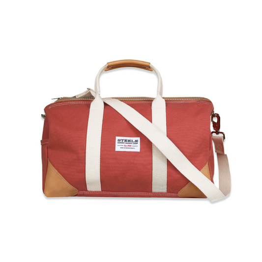 Red duffel bag with white straps and brown accents on a white background