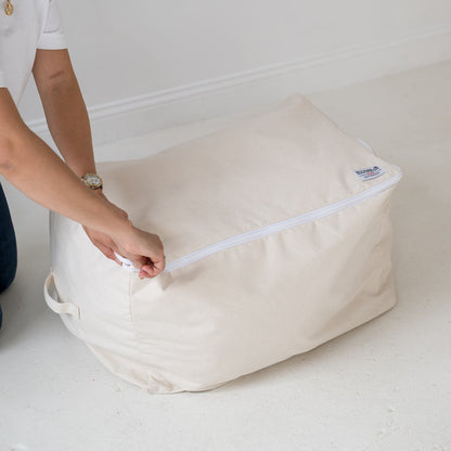 Person zipping a large beige storage bag on a white surface