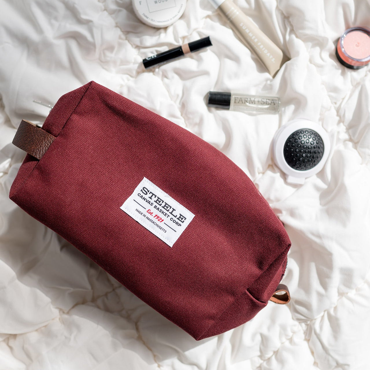 Maroon toiletry bag with cosmetic products on a white textured surface