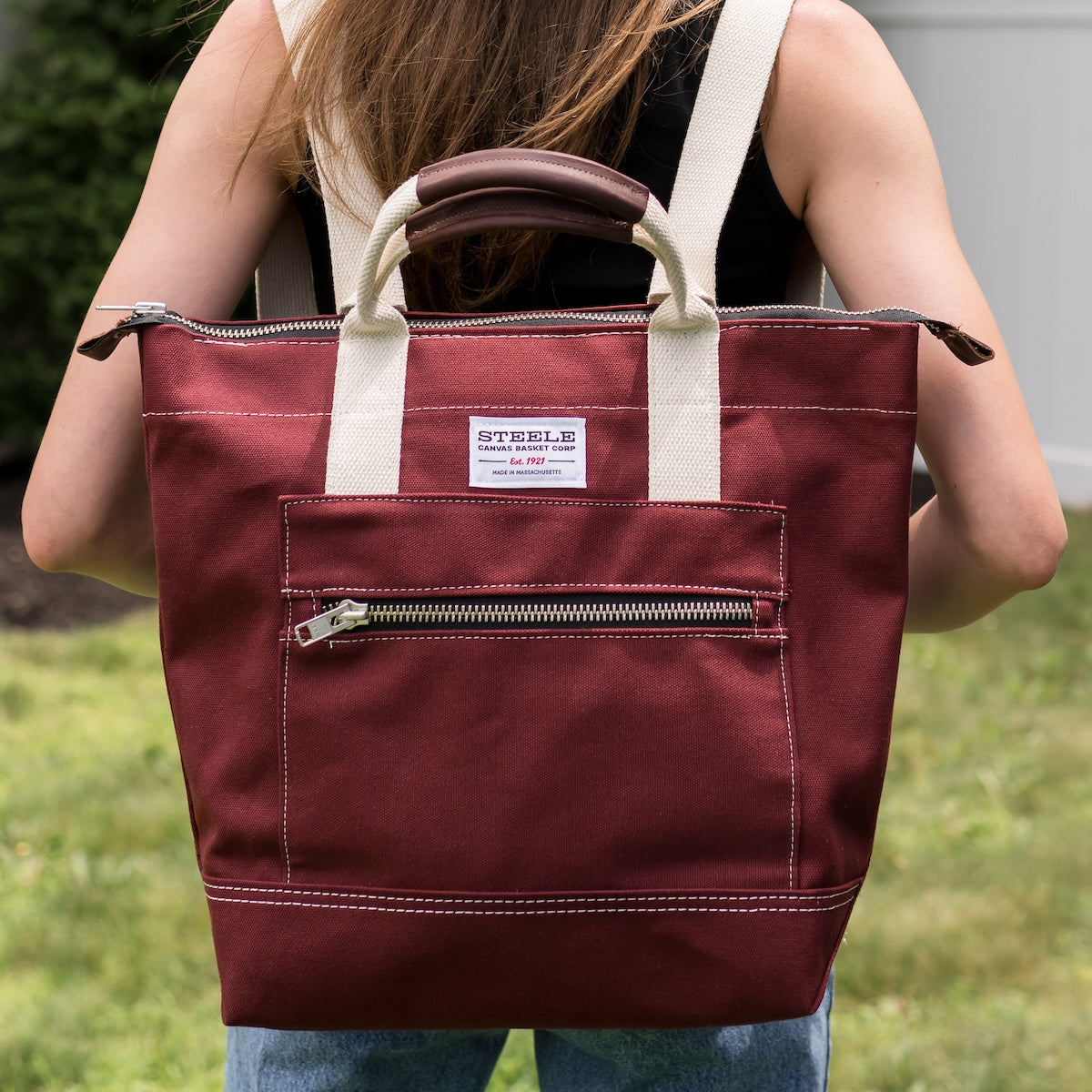 Person holding a maroon tote bag with a visible brand label outdoors.