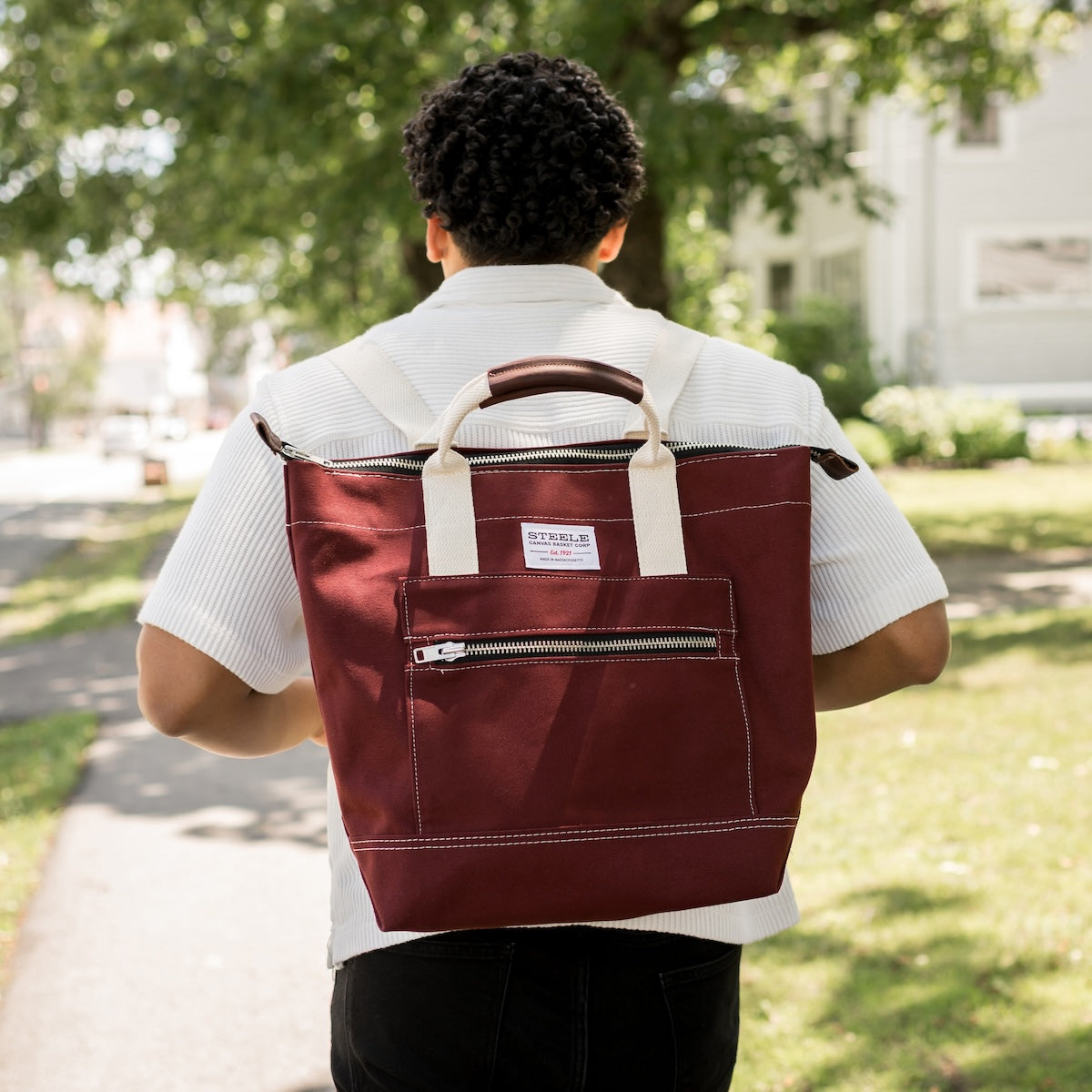 Person wearing a maroon backpack with a visible brand label outdoors.