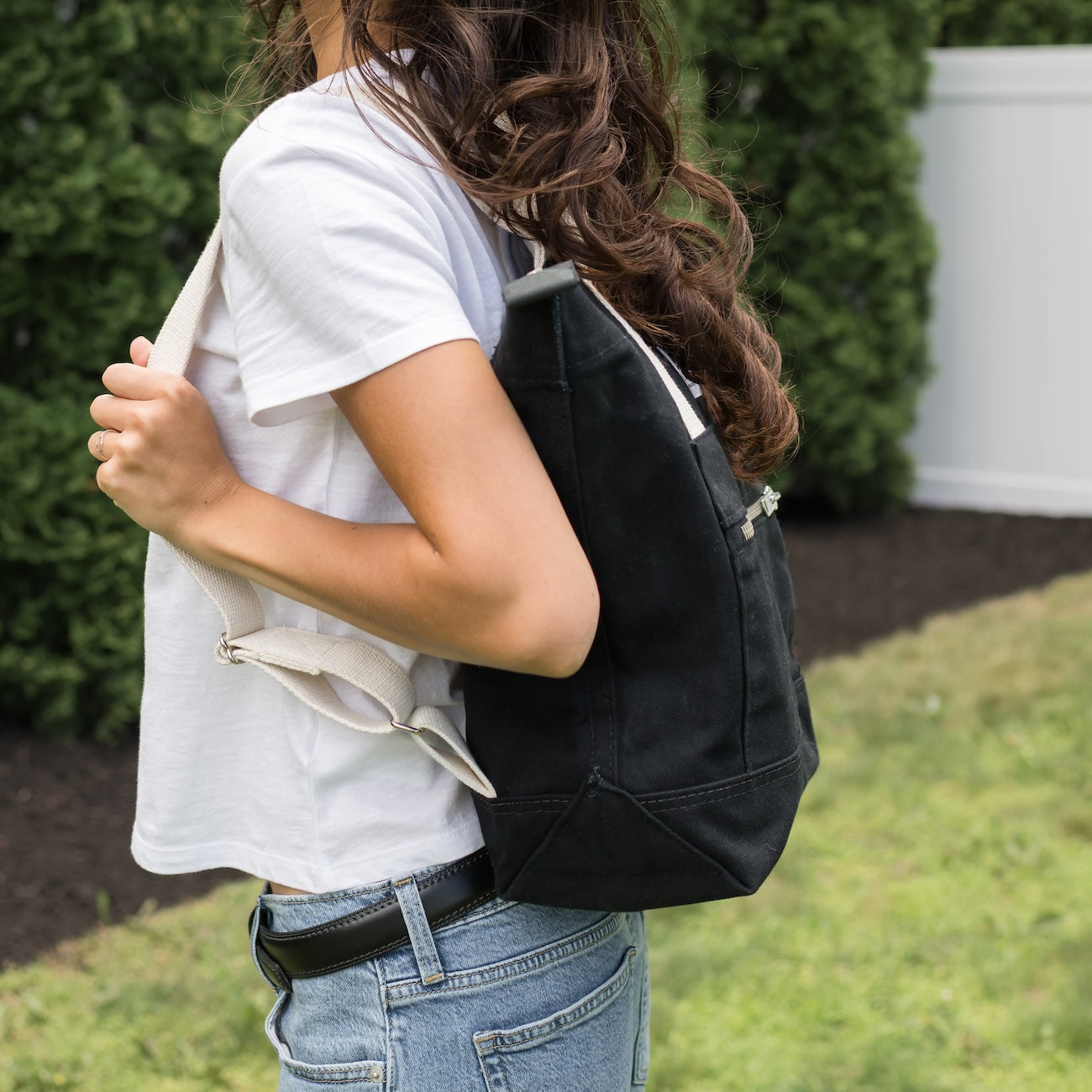 Person wearing a black backpack outdoors with greenery in the background