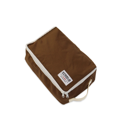 A brown fabric shoe bag with cream-colored piping and a top zipper, featuring a white label with Steele Canvas branding.